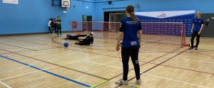 A goalball game taking place with #FindTheNext Goalball Academy players. Chelsea Hudson is looking on as a referee.