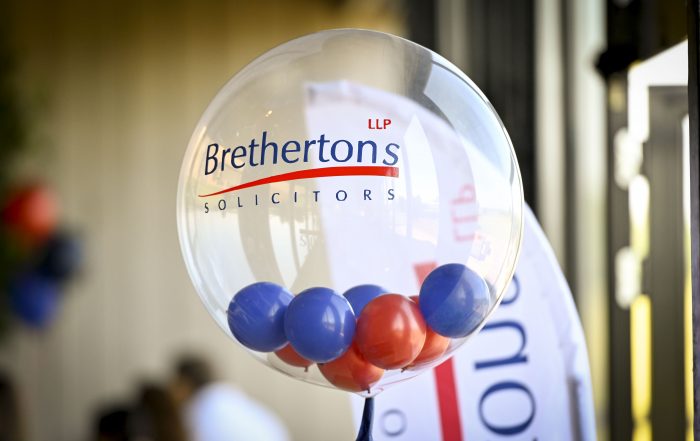 A clear round balloon with the Brethertons LLP Solicitors logo on in blue and red. The balloon is filled with red and blue balls