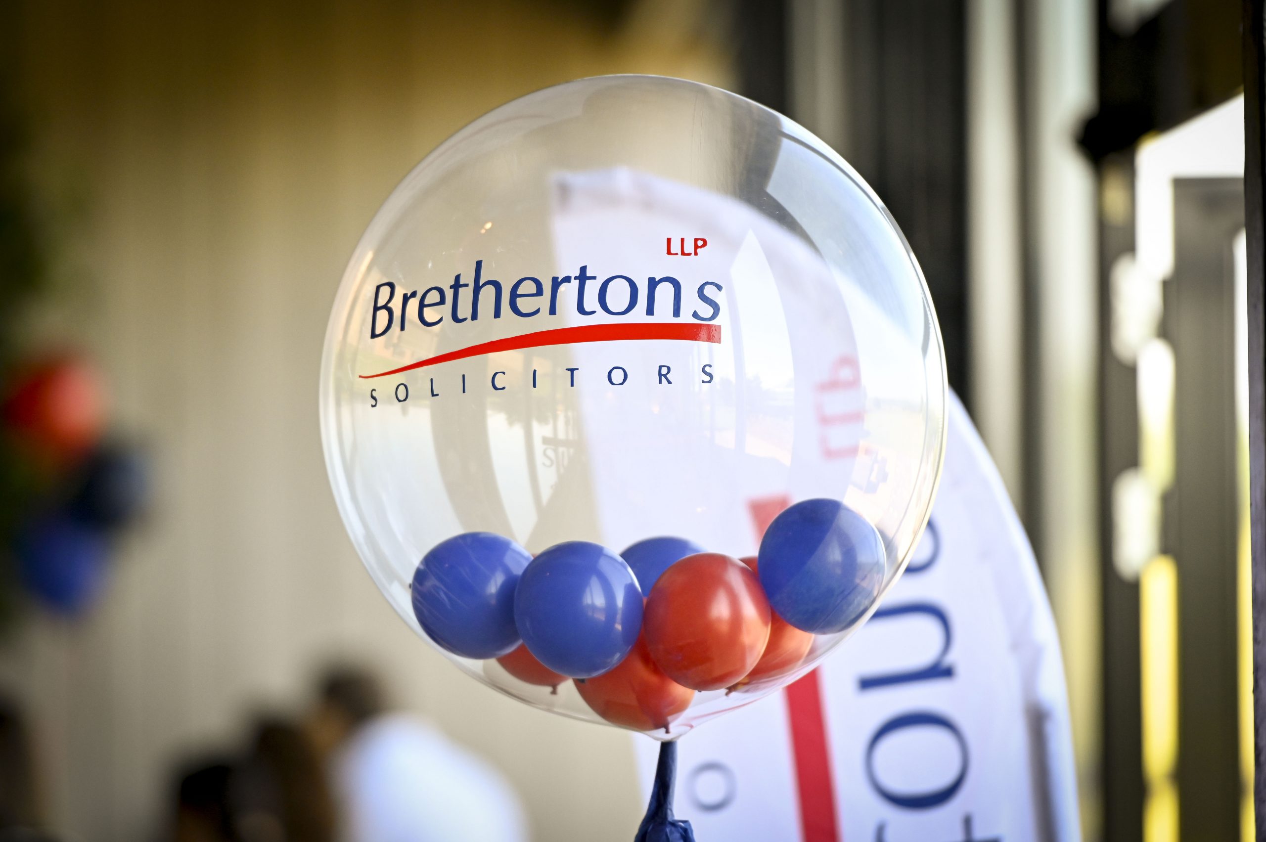 A clear round balloon with the Brethertons LLP Solicitors logo on in blue and red. The balloon is filled with red and blue balls