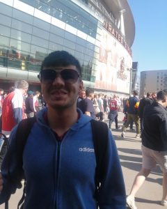 Mustafa Abbas standing outside Emirates Stadium for an Arsenal game in a blue hoodie, with a massive smile with cool sunglasses!