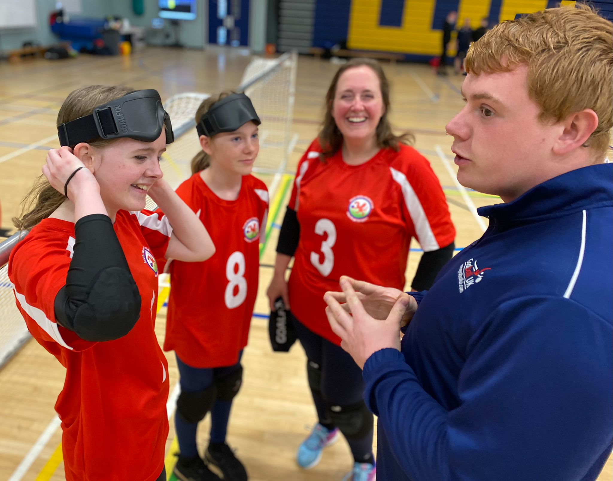 Three female South Wales goalball team members stand talking to Chris. He is wearing a blue Goalball UK top. A purple square with the 'This Girl Can' logo is in the bottom left of the image.