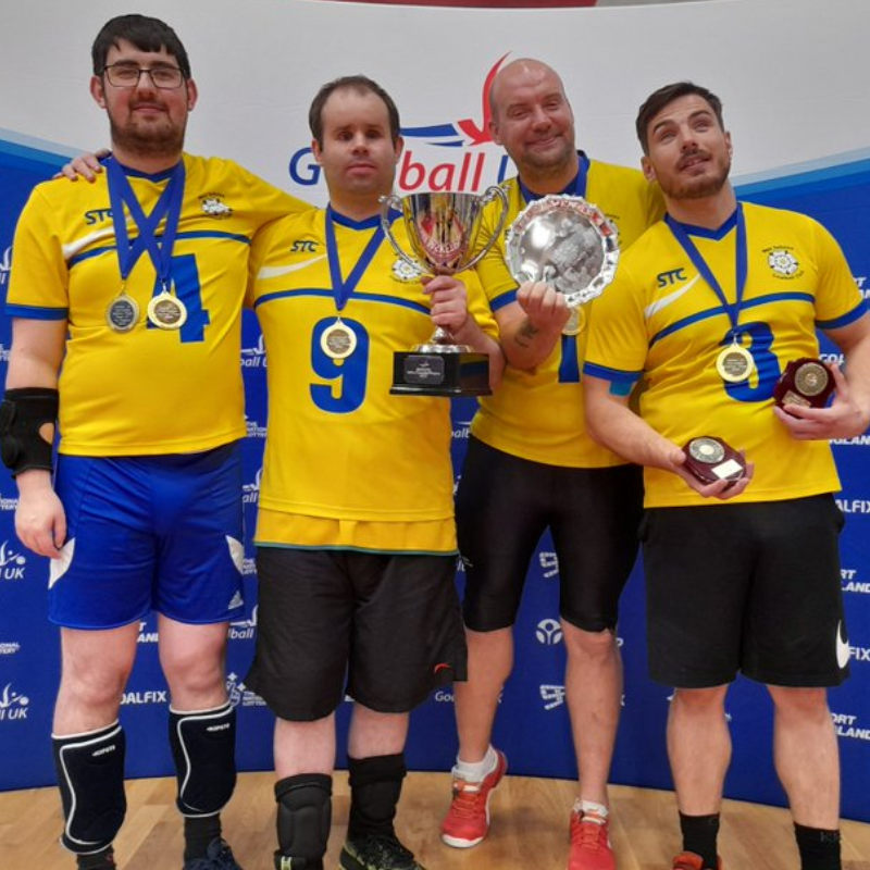 West Yorkshire Goalball Club team photo with four players including Nick. They are holding up their medals and a trophy