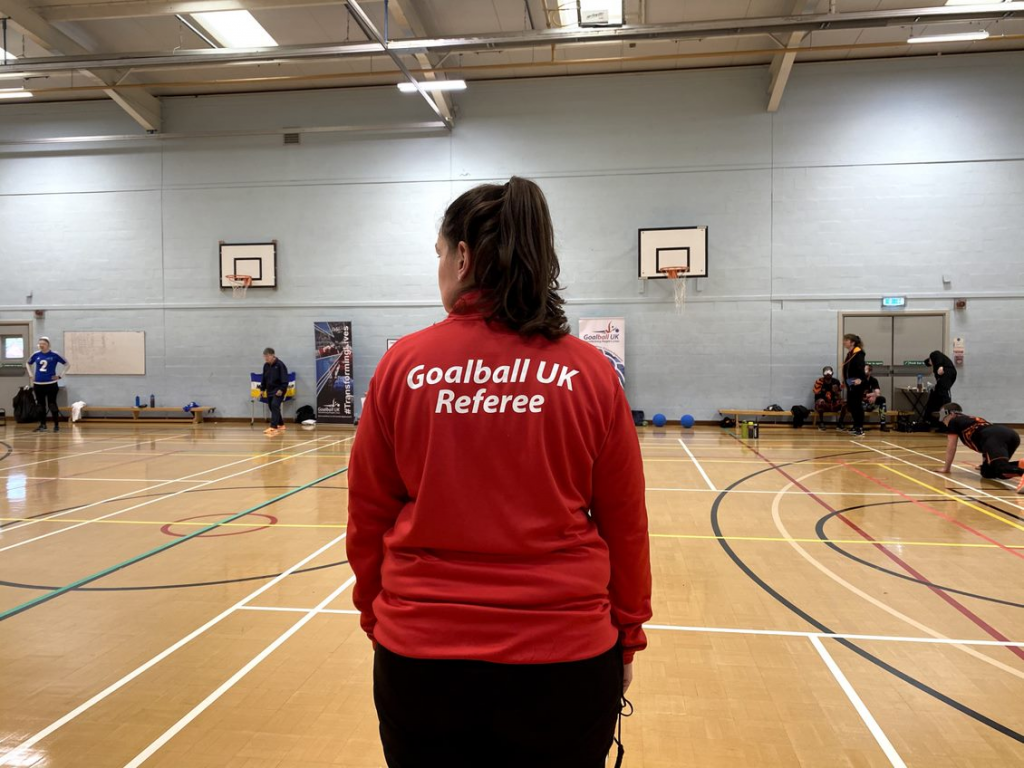 Dani Dillon in a red Goalball UK referee top overseeing the game