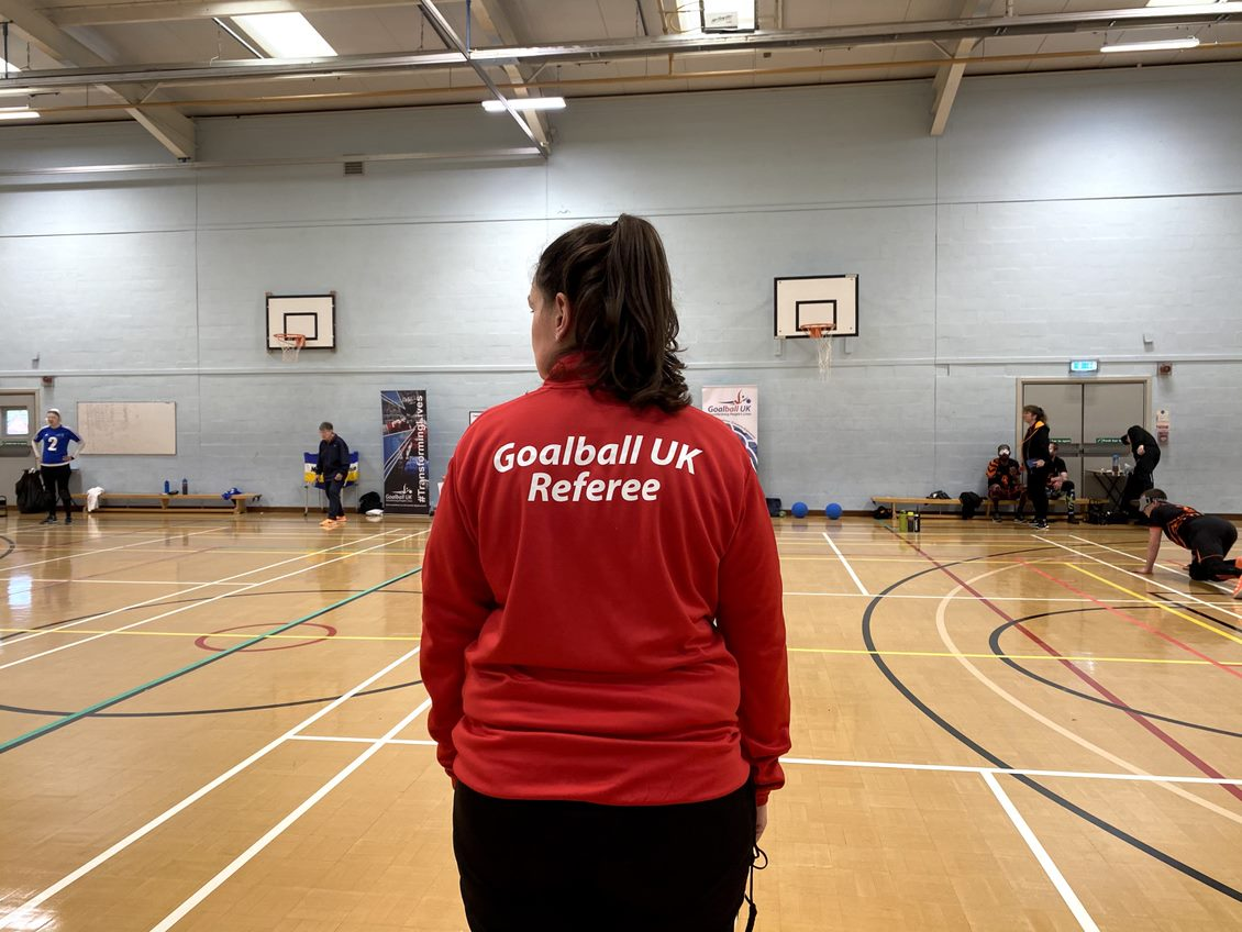 Dani Dillon in a red Goalball UK referee top overseeing the game