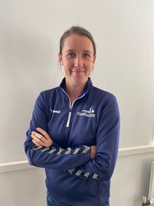 Faye Dale portrait, Faye is wearing a blue Goalball UK zip jumper and is stood infront of a white wall