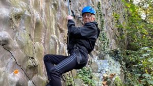 Harry has a go at abseiling. He is wearing a helmet and smiling at the camera.