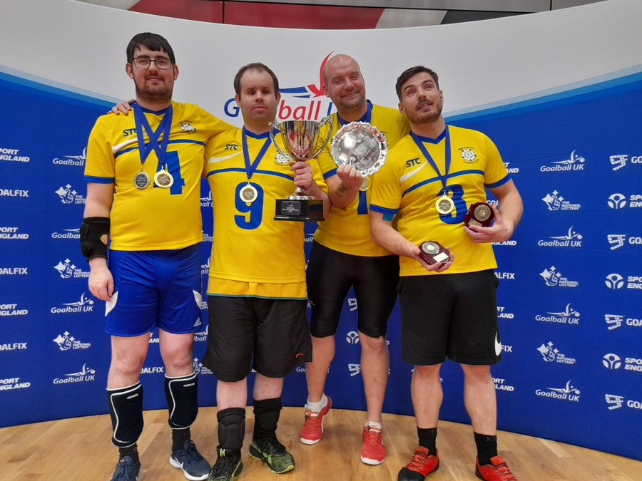 West Yorkshire Goalball Club team photo with four players including Nick. They are holding up their medals and a trophy