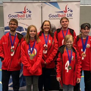 South Wales goalball club members stand in front of a Goalball UK branded pop up banner and smile for a group photo