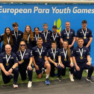 Group photo of Aaron and the whole team at the European Para Youth Games. Everyone is wearing blue Goalball UK kit and wearing their bronze medals.