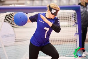 A female GB goalball player on court at the world championships with the ball. She is ready to throw it into play.