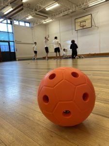 A close up photo of a junior goalball with people stretching in the background in a sports hall