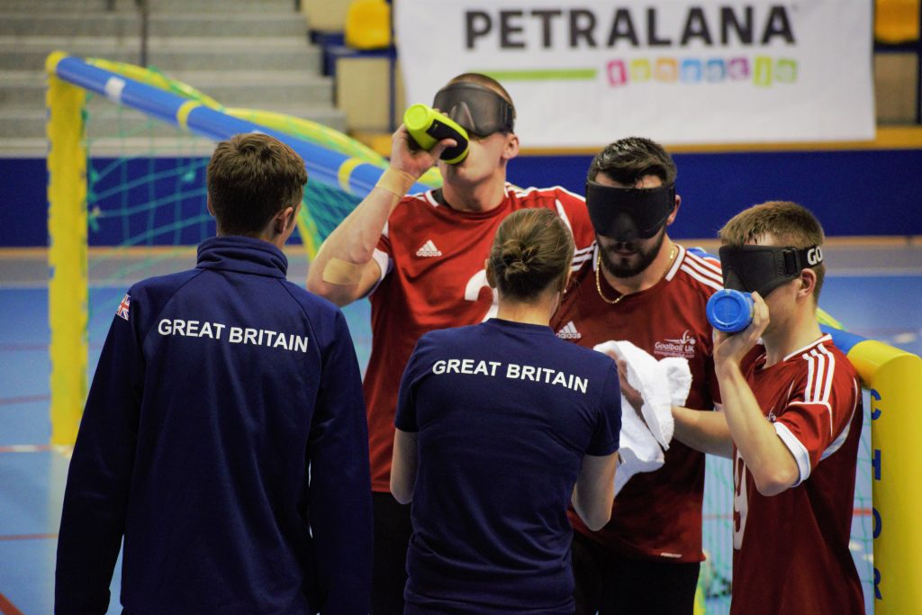 Group photo of GB Men in a timeout with coaches Faye and Alex talking to the squad.