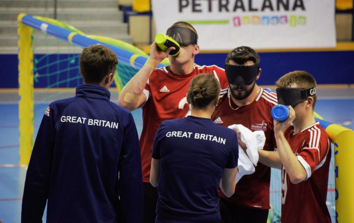 Group photo of GB Men in a timeout with coaches Faye and Alex talking to the squad.