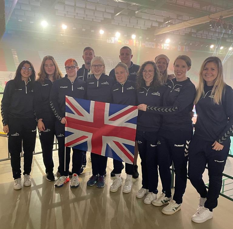 GB Women's squad standing together in navy blue tracksuits at the iBSA World Championships closing ceremony, proudly holding a GB flag!