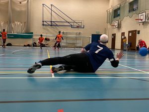Dave Scott of Winchester Kings diving to save a goalball for Winchester Kings. The ball is flying across the hall to the right of Dave's hands.