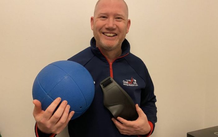 Mark Winder is stood holding a blue goalball and black eyeshades. He is smiling for the camera and wearing a blue Goalball UK top.