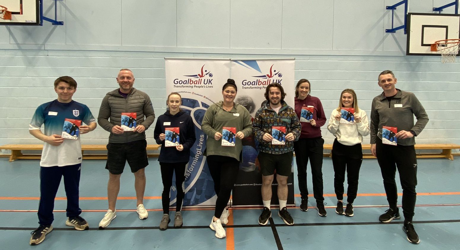 All 8 newly passed candidates on the Goalball School Leaders Course held at The Hive, Birkenhead. All candidates are stood smiling, holding their certificates, in front of two Goalball UK logo banners.