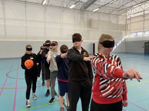 Action shot of the Goalball School Leaders, with the candidates practicing their communication and teamwork skills in a game of ‘Over and Under’ wearing eyeshades.