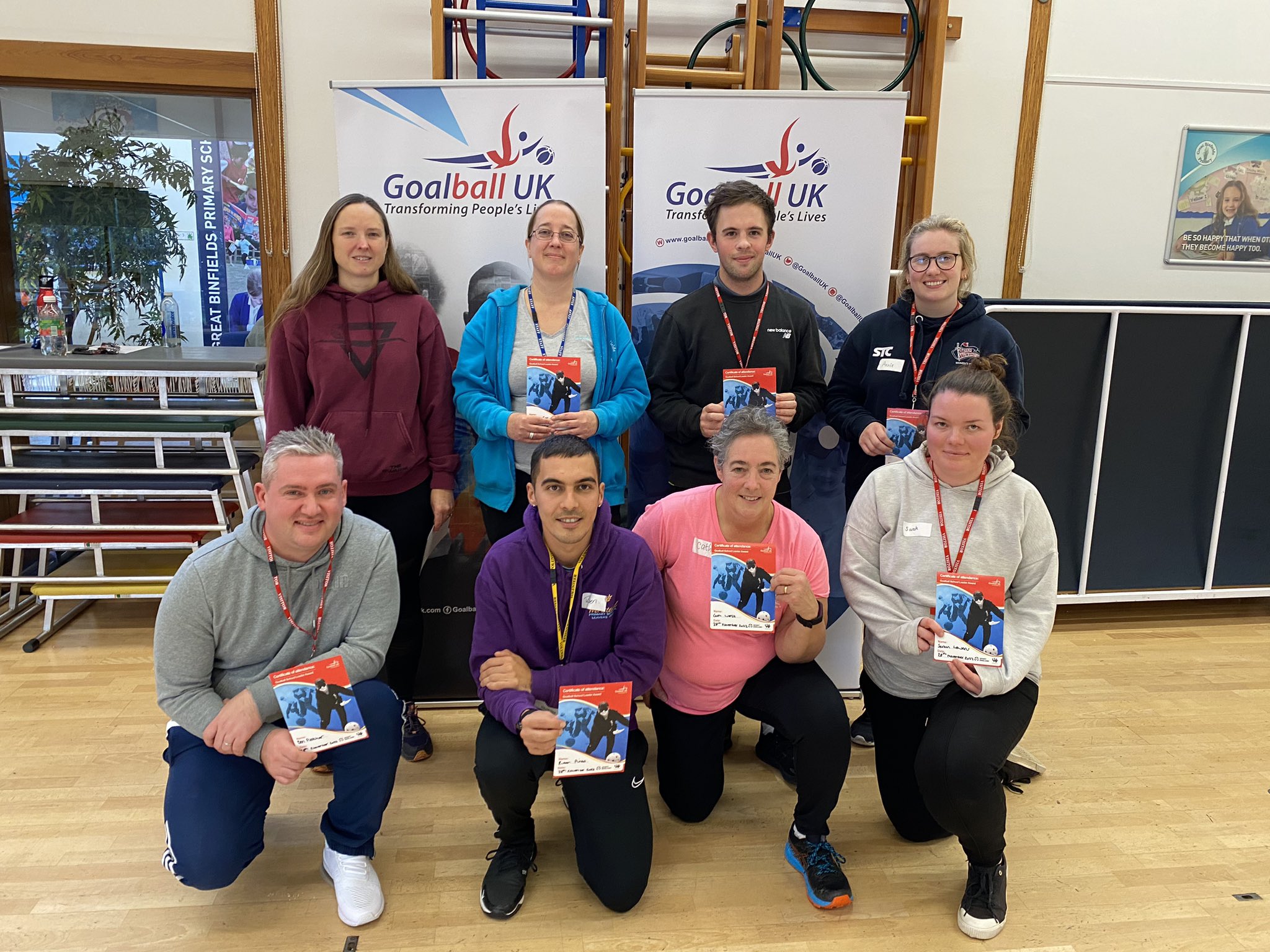 Group photo of the 8 candidates on the Hampshire Goalball School Leaders Course. The group are in two rows of four, with the front row knelt down, smiling and holding their certificates. The group is also stood in front of two Goalball UK logo banners.