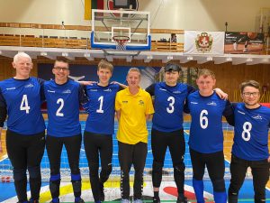 GB Men and Stephen Newey pose for a group photo. GB Men are wearing blue kit and Stephen is wearing a yellow t-shirt and is in the centre of the photo