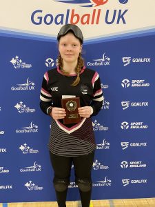 Chelsea Hudson stands with her award and poses for a photo against a Goalball UK branded banner