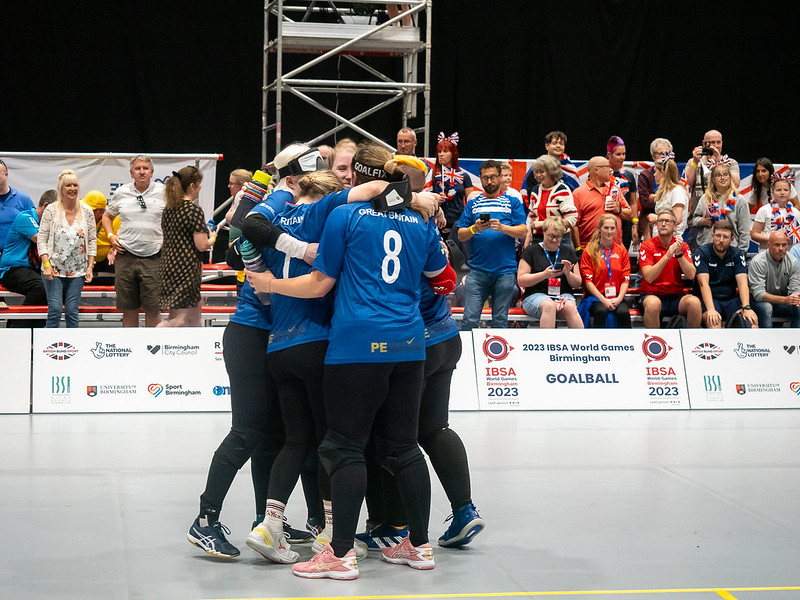 GB Women huddle together for a group hug after a game whilst the crowd watches on from the stands