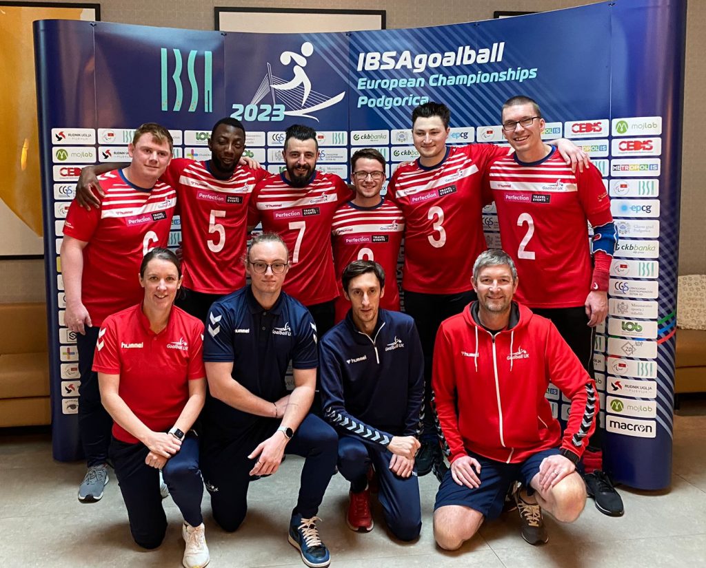 GB Men's goalball athletes pose for a group photo standing with their coaches and staff kneeling in front of them