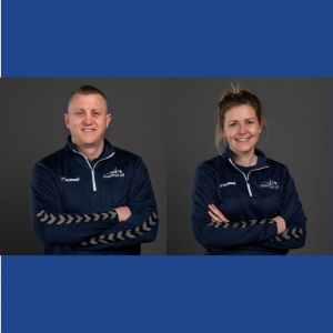 Aaron Ford and Becky Ashworth side by side for their Great Britain profile headshot. They are both smiling to the camera wearing navy blue Goalball UK jackets, in front of a dark grey photoshoot banner.