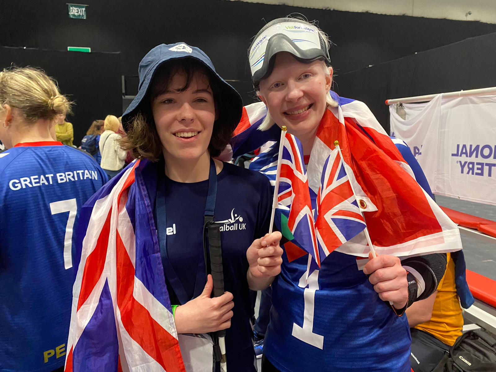 Sarah Leiter stands for a smiley photo with her team mate from Cambridge during the 2023 IBSA World Games. Sarah is dressed in GB kit and has a union jack draped around her and her friend