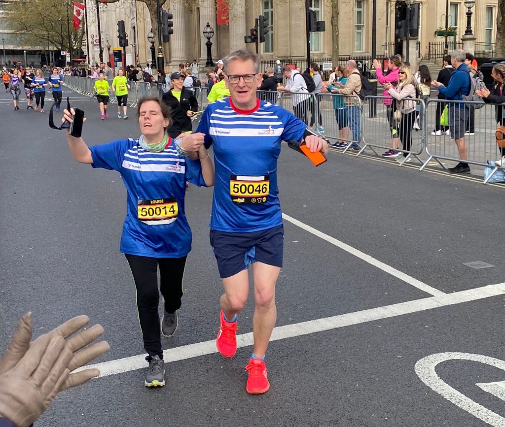 Louise runs the London Landmarks Half Marathon 2024 with guide Justin. They both wear blue and white Goalball UK tops and yellow race numbers