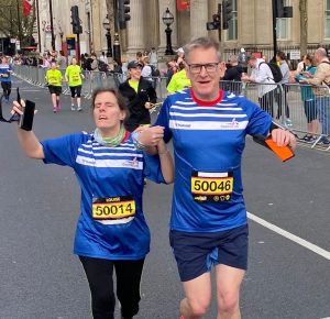 Louise runs the London Landmarks Half Marathon 2024 with guide Justin. They both wear blue and white Goalball UK tops and yellow race numbers