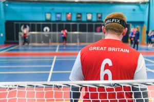 Photo taken from behind a goalball goal with Chris Colbert looking towards the other end of the court, wearing a red GB shirt.