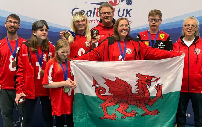 Group pic of the South Wales Goalball Club - they are all wearing red jerseys and holding up the flag of Wales