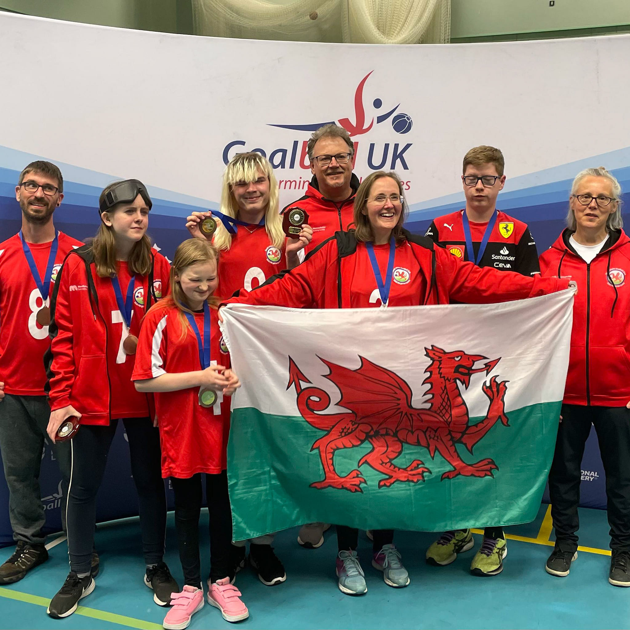 Group pic of the South Wales Goalball Club - they are all wearing red jerseys and holding up the flag of Wales