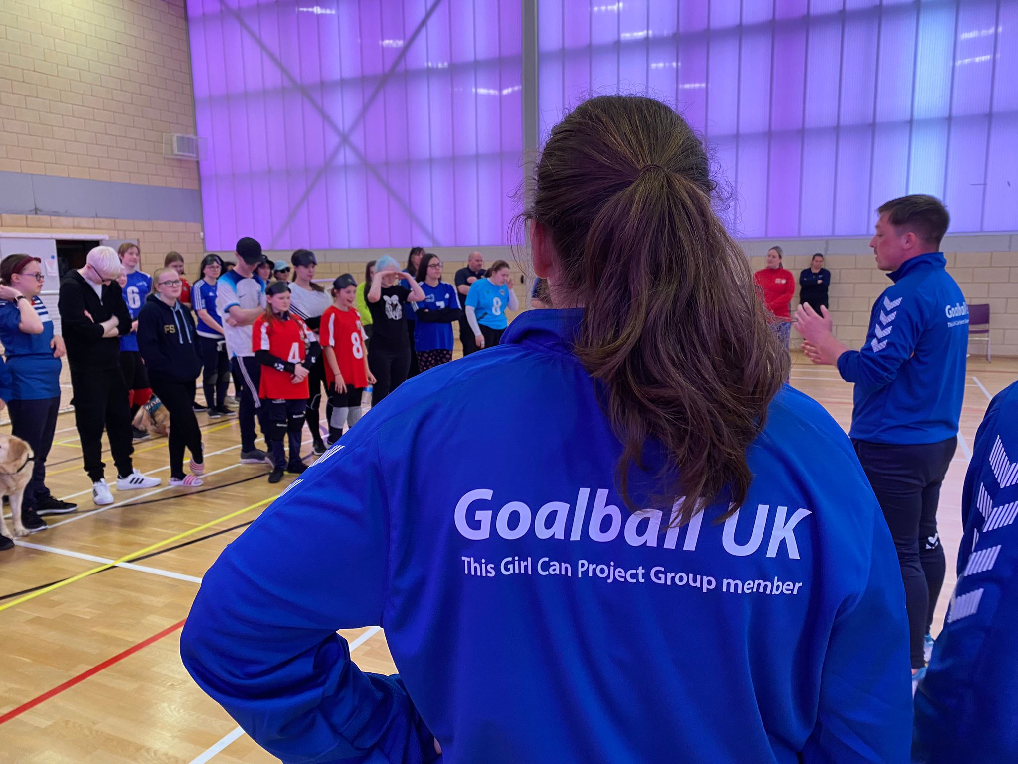 WhatsApp Image 2024-04-30 at 15.27.05 Lois Turner of the This Girl Can Project Group standing in a blue jacket. The camera is just behind her showing her watching the opening presentation of the competition.