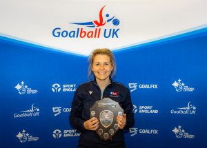 Becky Ashworth with her award in front of a Goalball UK banner.