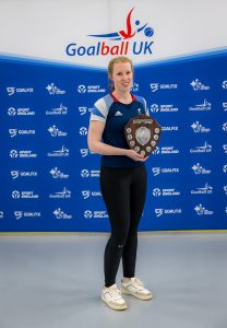 Georgie Bullen with her award in front of a Goalball UK banner.