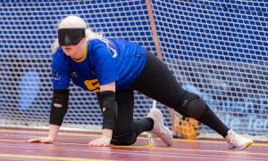 A female player for Winchester Goalball Club on court during a goalball game. They are in their ready position with the goal behind them.