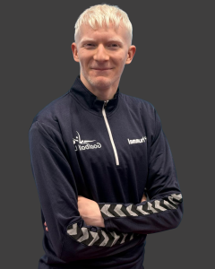 Leo Stubbs Performance profile photo. Leo is standing with his arms folded wearing a navy blue Goalball UK quarter zip jacket. There is a grey background behind him.