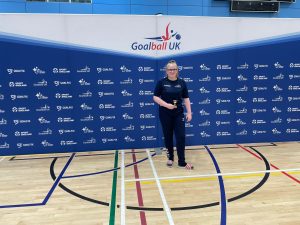 Faith Stubbs, the first ever Academy Phoenix Award winner standing in front a big Goalball UK banner. Faith is wearing a navy blue Goalball Academy tracksuit.