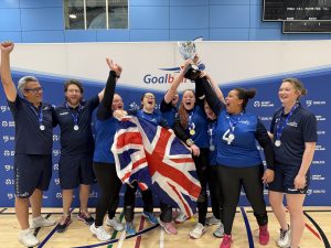 Group photo of GB women celebrating by lifting the trophy and waving a union jack flag