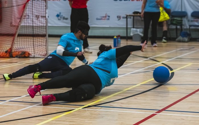 A female player for Birmingham Goalball Club diving to save a shot during a game. She is wearing a light blue jersey and is playing in the centre position.