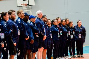 Great Britain Men and Women standing together in a line, side by side, at the opening ceremony of the IBSA goalball European A Championships. Everyone is wearing navy blue Great Britain jackets, tracksuit bottoms or shorts.
