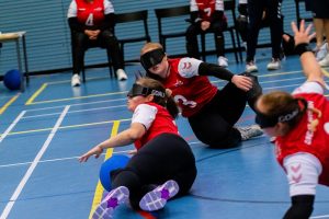 All 3 women's players on court (left - Kali Holder, centre - Lois Turner, right - Chelsea Hudson) dive to save the ball. Lois in centre has collected it, with Kali and Chelsea diving behind her as backup!
