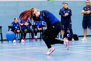 Chelsea Hudson throwing a goalball during a game. She is wearing her blue GB shirt, and her ginger hair with pink highlights is in a ponytail, which is flicking up past her head, making a cool effect as she releases the ball.