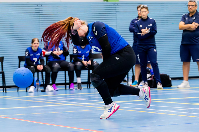 54828229615_18da5ebbc5_c Chelsea Hudson throwing a goalball during a game. She is wearing her blue GB shirt, and her ginger hair with pink highlights is in a ponytail, which is flicking up past her head, making a cool effect as she releases the ball.