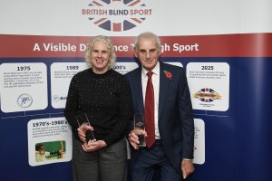 Kathryn and Clive, stood in front of a British Blind Sport banner, proudly holding their awards which are made out of glass and engraved with their names.