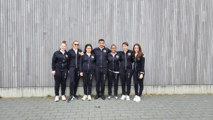 GC Golden Flash squad photo, all 7 team members are standing outside in black tracksuits with their arms around one another.