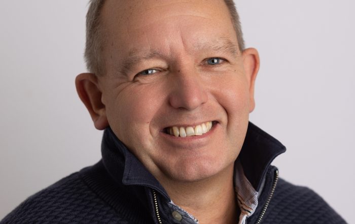 Profile photo of Ian Clarke, who is smiling brightly to the camera whilst wearing a navy three quarter zip formal jacket.