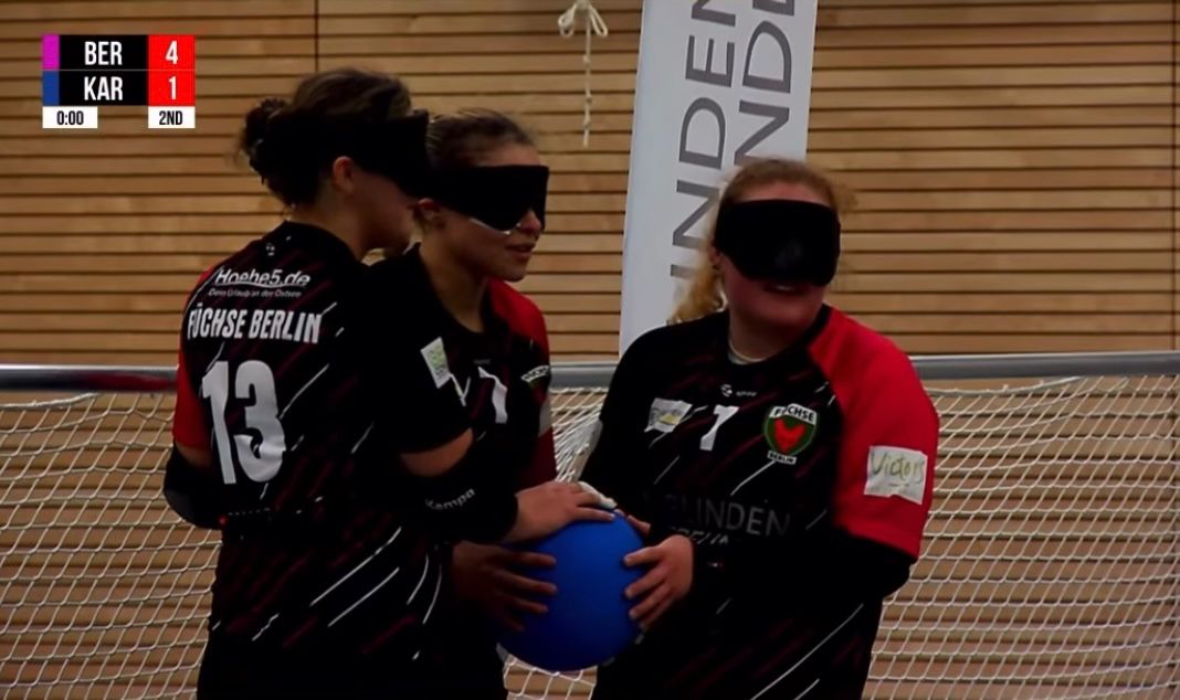 Kali Holder and her Berlin teammates standing at back centre on court, during a game. There is less than a second left in the game, so everyone has a hand on the ball as they're not going to throw it.